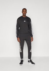 Sweatshirt com gola crew preta e calças de fato coordenadas, com riscas brancas nas mangas e lados, feitas de um tecido suave com um corte atlético.
