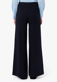 Pantaloni in maglia a gamba larga di colore blu navale con vita a costine e texture liscia, caratterizzati da una vestibilità morbida che scende dai fianchi fino a terra.