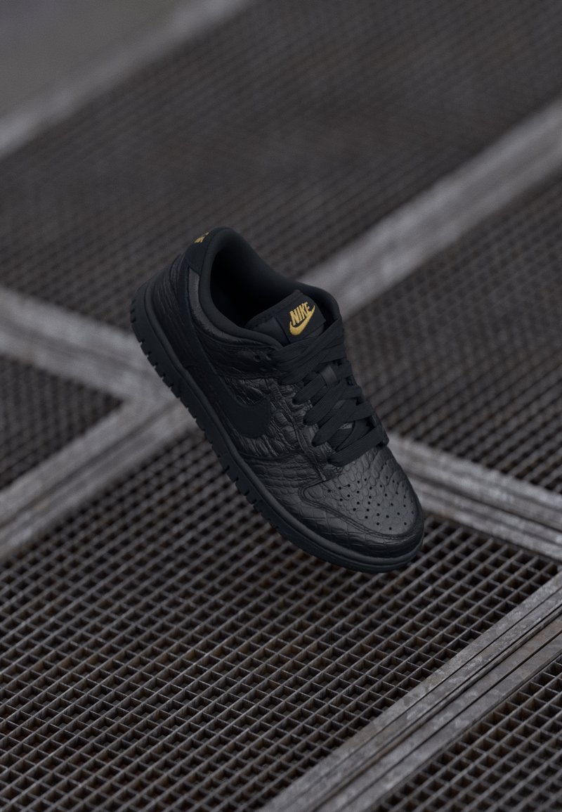 Juodas Nike sportbačius su tekstūruota odos viršumi, geltonais logotipo akcentais, perforuota pirštų dėžute ir plokščiais juodais raišteliais. Įrengtas guminiu padu.