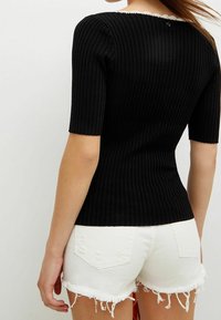 Top noir à côtes avec des manches courtes et un col accentué de dentelle, associé à un short en denim blanc déchiré avec des bords effilochés.