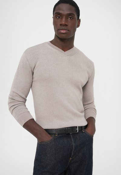 Svijetlo sivi rebrasti pulover s V-izrezom, dugim rukavima i prilagođenim krojem, upareni s tamnim trapericama i crnim remenom.