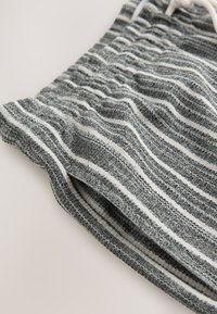 Primo piano di tessuto lavorato a maglia a righe grigie e bianche con una cintura elastica e un laccetto bianco.