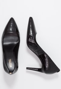 Talons hauts en cuir verni noir avec un bout pointu, présentant une texture crocodile et un talon aiguille fin. Détail du logo en or à l'intérieur.