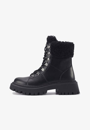 Mustad mustadjalatsid valebucki mansetiga, nahast keha, metallist nöörimise detailid ja paks, tekstureeritud kummitald.