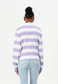 Purple and white striped sweatshirt with a relaxed fit, long sleeves, and ribbed cuffs, paired with light blue jeans.