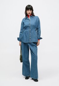 Τζιν μπουφάν με κουμπιά, συνδυασμένο με τζιν παντελόνια με φαρδιά μπατζάκια. Και τα δύο είναι ανοιχτό μπλε, με άνετη εφαρμογή και λεία υφή.