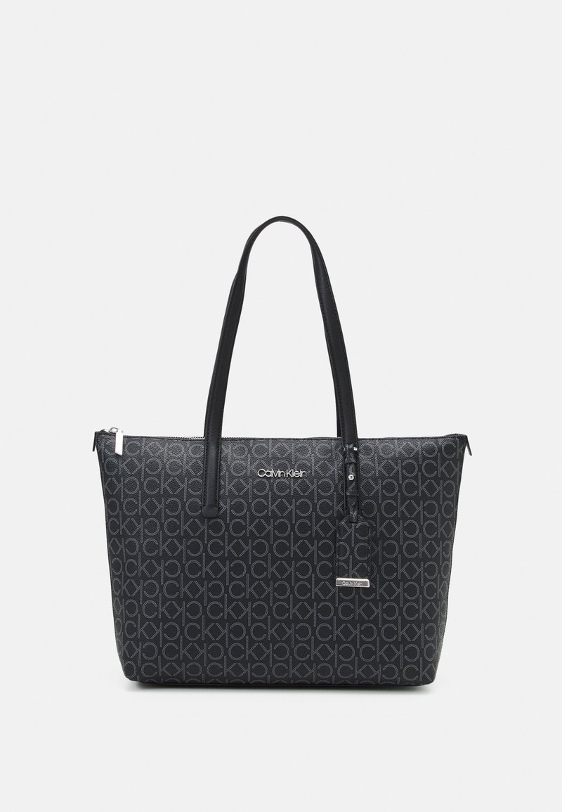 Sac cabas noir Calvin Klein avec motif logo CK répétitif, doubles anses d’épaule et petite étiquette suspendue avec le nom de la marque.