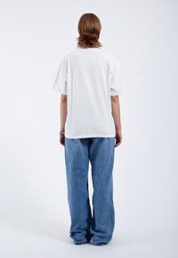 T-shirt en coton blanc à coupe décontractée, associé à un jean en denim bleu clair ample. Design simple, sans motifs ni accents visibles.