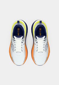 Valged sportlikud kingad oranžide ja tumesiniste aktsentidega, tekstureeritud võrkkangas pealisosa, pehmendav tald ja erksad kollased detailid kaela ümber.