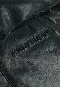 Nahaufnahme eines schwarzen Lederhandschuhs mit geprägtem "PME LEGEND"-Text und sichtbaren Nahtdetails.