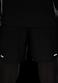 Calções desportivos pretos com textura suave, apresentando duas riscas horizontais brancas na frente. Design simples, corte até ao joelho.