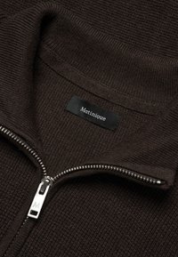 Pull en tricot brun foncé avec une fermeture éclair argentée partielle et une étiquette noire portant l'inscription "Matinique" à l'intérieur du col.