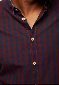 Camisa de botones con rayas verticales rojas y azul marino, diseño con cuello, que presenta botones de color claro y detalles de costura visibles.