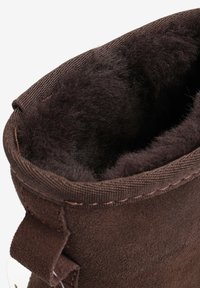 Brązowy zamszowy but z miękką, pluszową wyściółką wewnętrzną. Kołnierz ozdobiony jest podszyciem z przeszyciem oraz małą, materiałową pętelką po boku.