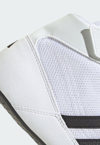 White athletic shoe featuring a mesh upper, smooth leather accents, black stripes, and a flexible rubber sole with textured detailing.