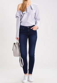 Randig off-shoulder-blus med volangkanter, tillsammans med mörkblå skinny jeans och vita sneakers. Outfiten kompletteras av en grå handväska.