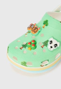 Hellgrüner Clog aus flexiblem Material, mit ausgestanzten Löchern, Cartoon-Figuren-Dekorationen und bunten Baum-Mustern auf der Oberfläche.