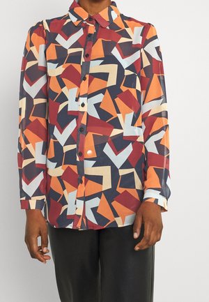 Kolorowa bluzka z geometrycznymi wzorami w czerwieni, pomarańczy, granacie, beżu i jasnym błękicie. Posiada kołnierzyk i zapięcie na guziki.