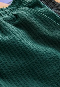 Pantalon à taille élastique vert foncé avec tissu texturé en maille gaufrée, montrant des détails en gros plan du matériau et des coutures.