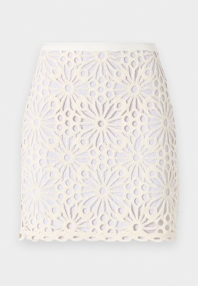 Fehér csipke mini szoknya virágmintákkal és kivágott részletekkel. A szoknya szegélye hullámos, a derékrész sima és enyhén fényes.