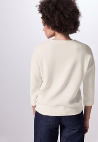 Lichtcrème, geribbelde gebreide shirt met driekwart mouwen en een ontspannen pasvorm. De achterkant heeft een ronde halslijn en een zoom die zachtjes gebogen is.