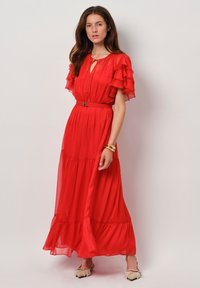 Rode maxi-jurk van vloeiende stof met gelaagde volants, sleutelgat-halslijn, cinched taille met een riem en een subtiele glans.