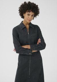Robe en denim foncé avec un col, des manches longues, une fermeture éclair à l'avant et deux poches poitrine. Présente une coupe droite et des accents dorés.