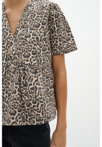 Top con stampa leopardata caratterizzato da scollatura a V, maniche corte a palloncino e orlo a peplum arricciato. Realizzato in tessuto morbido con un motivo testurizzato.