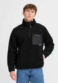 Black fleece pullover with a quarter-zip, textured fabric, zippered chest pocket, and side pockets. Simple design with no visible logos.