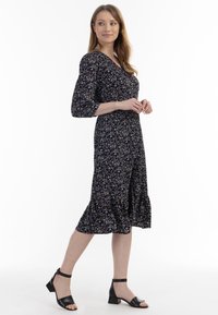Rochie midi florală, de culoare neagră, cu modele violet și alb. Dispune de mâneci tip puff, până la trei sferturi, și un tiv volanat. Asortată cu sandale negre cu toc.