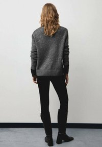 Maglione grigio con dettagli scintillanti, vestibilità comoda, polsini a coste, indossato con leggings neri e stivali neri alti, visto da dietro.