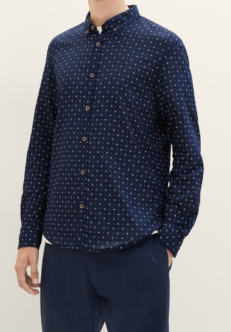 Mörkblå skjorta med vitt stjärnmönster, långa ärmar, krage med knappar och bruna knappar. Tillverkad av mjukt tyg med en slät yta.