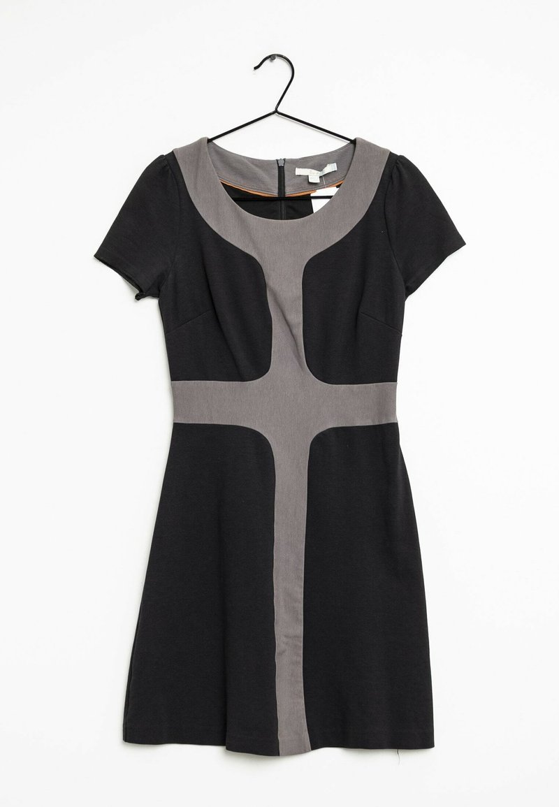 Svart kortärmad klänning med grått korsdesign på framsidan, rund halsringning och dragkedja bak, hängande på svart galje mot vit bakgrund.