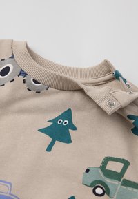 Beige trui met ronde halslijn, versierd met groene bomen, grijze auto's en blauwe accenten. Drukknopen op de schouder voor eenvoudig aan- en uittrekken.