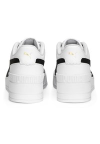 Paire de baskets blanches Puma avec des rayures noires, logo Puma doré au talon et semelles blanches épaisses, vues de dos sur fond blanc.