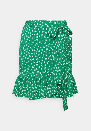 Groene wikkelrok met witte bloemenprint, gerimpelde zoom en een strik aan de zijkant, getoond op een effen lichte achtergrond.