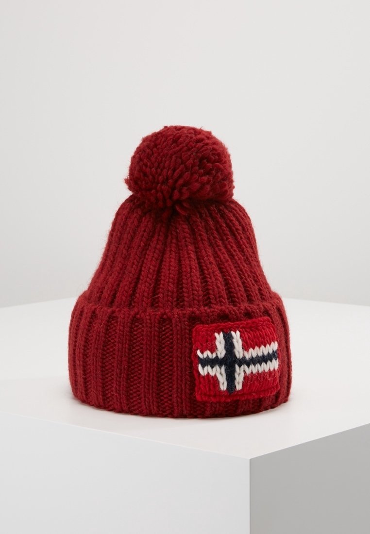 Bonnet d'hiver rouge en tricot avec pompon et un patch avec un motif de croix blanche, noire et bleue sur le bord avant.