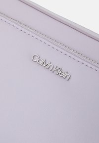 Portafoglio in pelle viola con finitura testurizzata, dotato di zip argentata e logo metallico "Calvin Klein".
