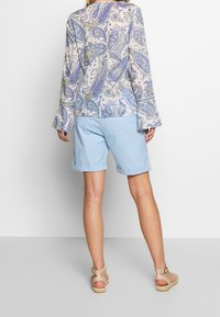 Shorts bleu clair et blouse à motifs avec des manches évasées. La blouse présente des motifs en paisley dans des teintes de bleu, jaune et blanc.