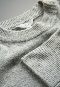 Suéter gris claro hecho de una tela texturizada. Cuenta con un cuello y puños de manga acanalados. Etiqueta visible con "THE SET" y talla "M."
