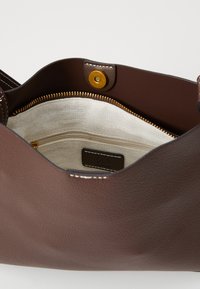 Brun skinnveske med en myk tekstur, som har en lukking med gullfarget spenne og et kremfarget stofffôr med en glidelåslomme.