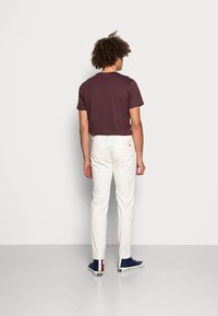 T-shirt corto bordeaux a maniche corte, pantaloni bianchi slim-fit e sneakers blu navy con dettagli marroni. Vestibilità casual, tessuto morbido, senza motivi visibili.