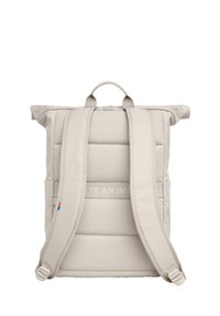 Sac à dos beige à rabat avec dos rembourré, bretelles réglables et une poignée supérieure. Présente un texte en relief subtil et des accents colorés.