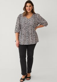 Leopardprint blouse in lichtbeige en zwart, met een V-hals, driekwart pofmouwen en een geplooide taille, gecombineerd met zwarte jeans.