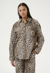 Camicia con stampa leopardata e bottoni, dotata di ampie tasche, realizzata in un tessuto liscio. Vestibilità over, con colletto classico e maniche lunghe.