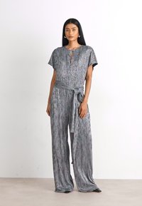 Grå mønstret jumpsuit med løs pasform, korte ærmer, en nøglehuludskæring og et matchende stofbælte knyttet om taljen.