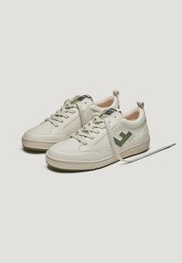 Baskets blanches en cuir avec des accents verts, bout rond, intérieur rembourré et semelle en caoutchouc texturé. Présente un logo et des lacets plats.