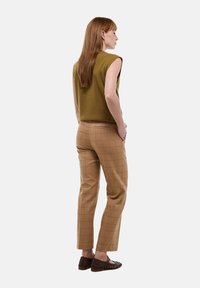 Haut en tricot sans manches vert olive associé à un pantalon à carreaux beige, offrant une coupe slim et un tissu texturé. Des chaussures tressées marron complètent le look.