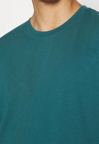T-shirt corto verde acqua, realizzato in morbido cotone con collo rotondo e texture liscia. Nessun motivo o grafica visibili.