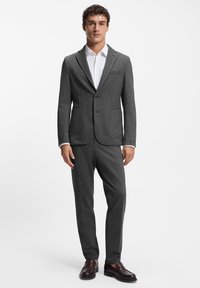Gray suit made of textured fabric, featuring a tailored blazer with two pockets, matching pants, and a white shirt underneath.